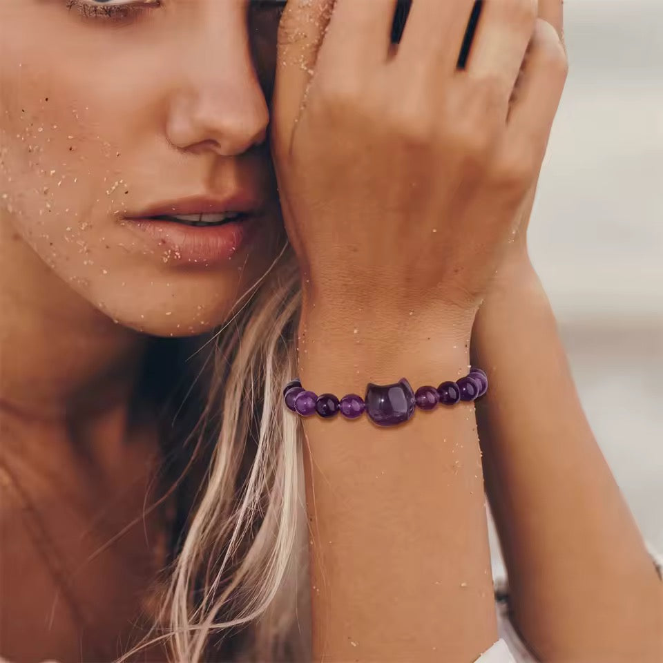 Close-up of a woman on the beach wearing a purple amethyst beaded stone bracelet with Cat Head accent bead.