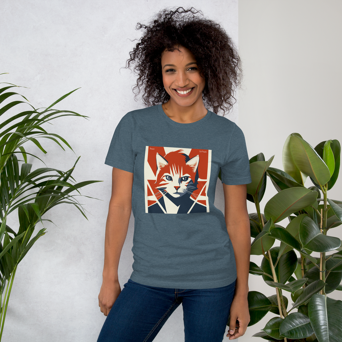 Woman with curly hair in front of a white background with plants. Her shirt is a cat themed Bowie album cover but it says Meowie.