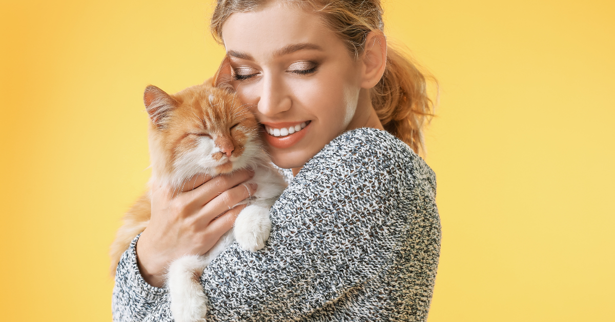 Woman hugging an orange cat against a yellow background