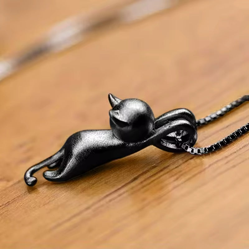 Black cat-shaped pendant on a chain against a wooden background