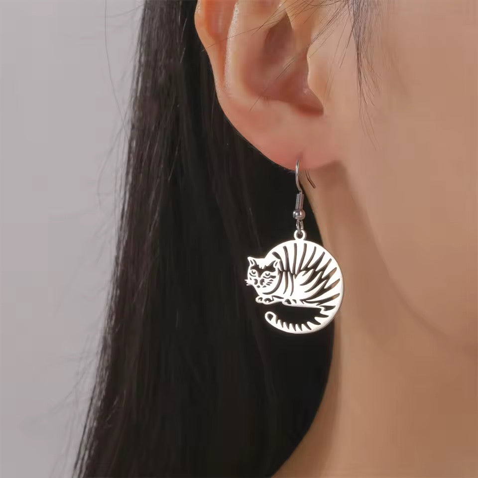 Silver curled up striped kitty dangles from an earring worn by a person with a neutral background