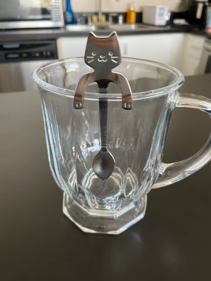 Clear glass mug with a cat-shaped stainless steel tea spoon on a kitchen counter