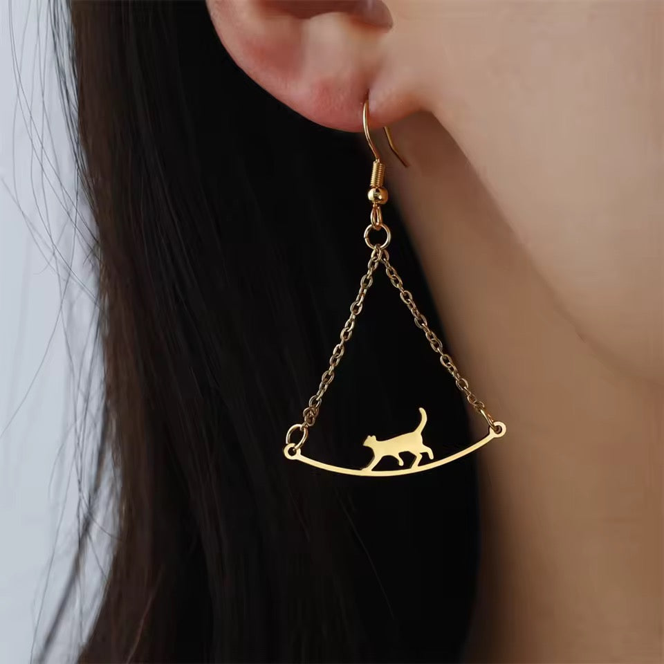 Gold Cat Walk earrings suspend a tiny cat from a chain. Connects to person with dark hair with a french wire.