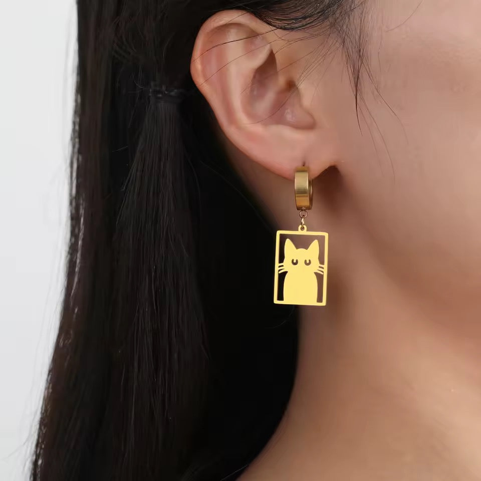 Gold hoop earrings feature a flat stainless cutout of a Cat in a Box on a person with dark hair