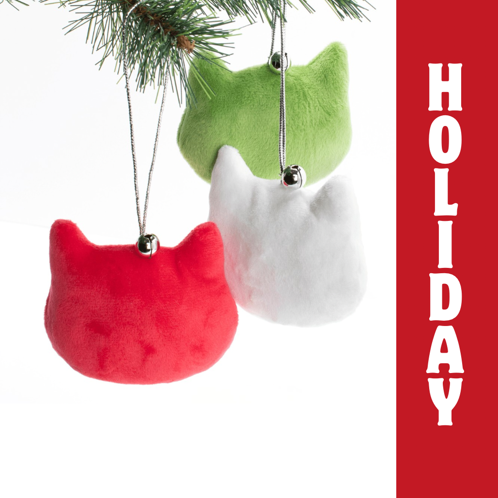 Three cat-shaped Christmas ornaments in red, green, and white hanging on a tree branch with 'HOLIDAY' text on a red background.