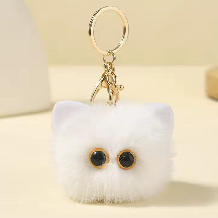 White fluffy Cat keychain with black eyes and a gold ring on a light background