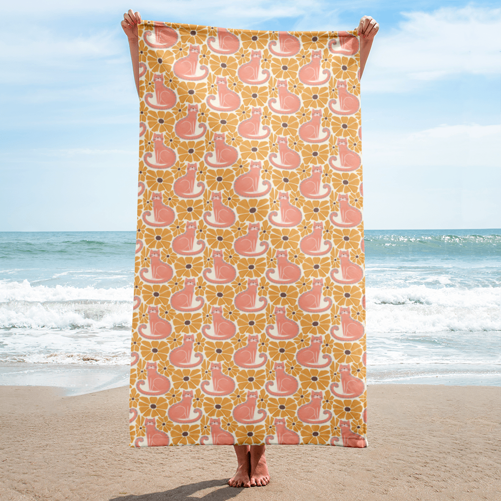 Person holding a beach towel with cat and flower pattern on a sandy beach.