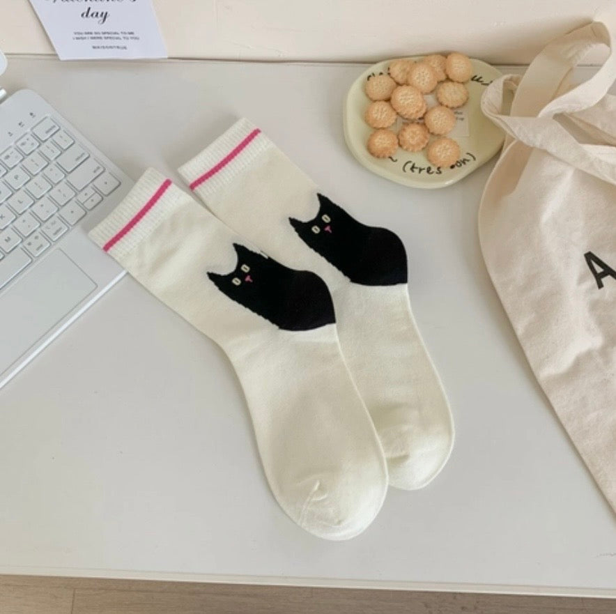 White socks with black cat designs on a desk with a keyboard and snacks.