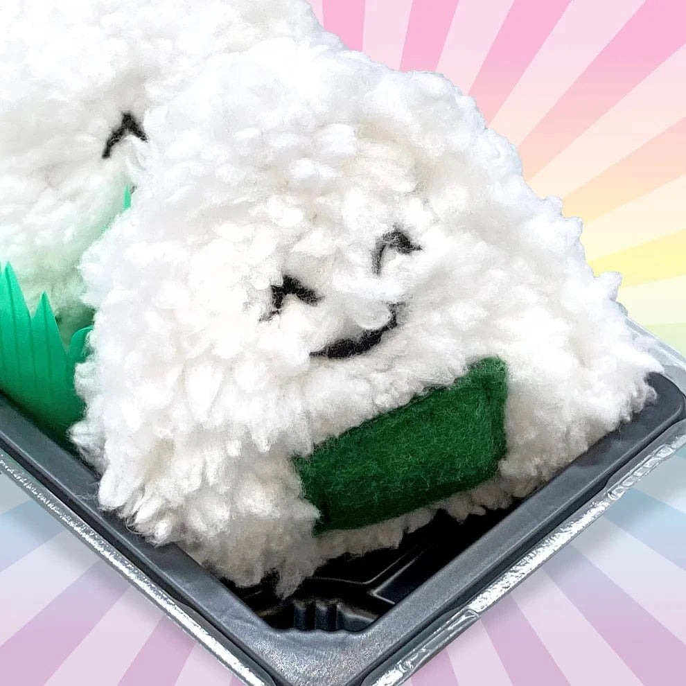 White plush sushi toy with black face and green base in a black container on a colorful background