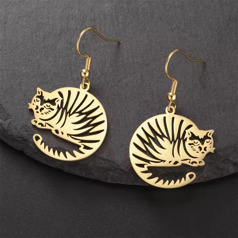 Gold disks feature a cutout cat with stripes made into adorable earrings dangling by a french wire on a dark stone surface