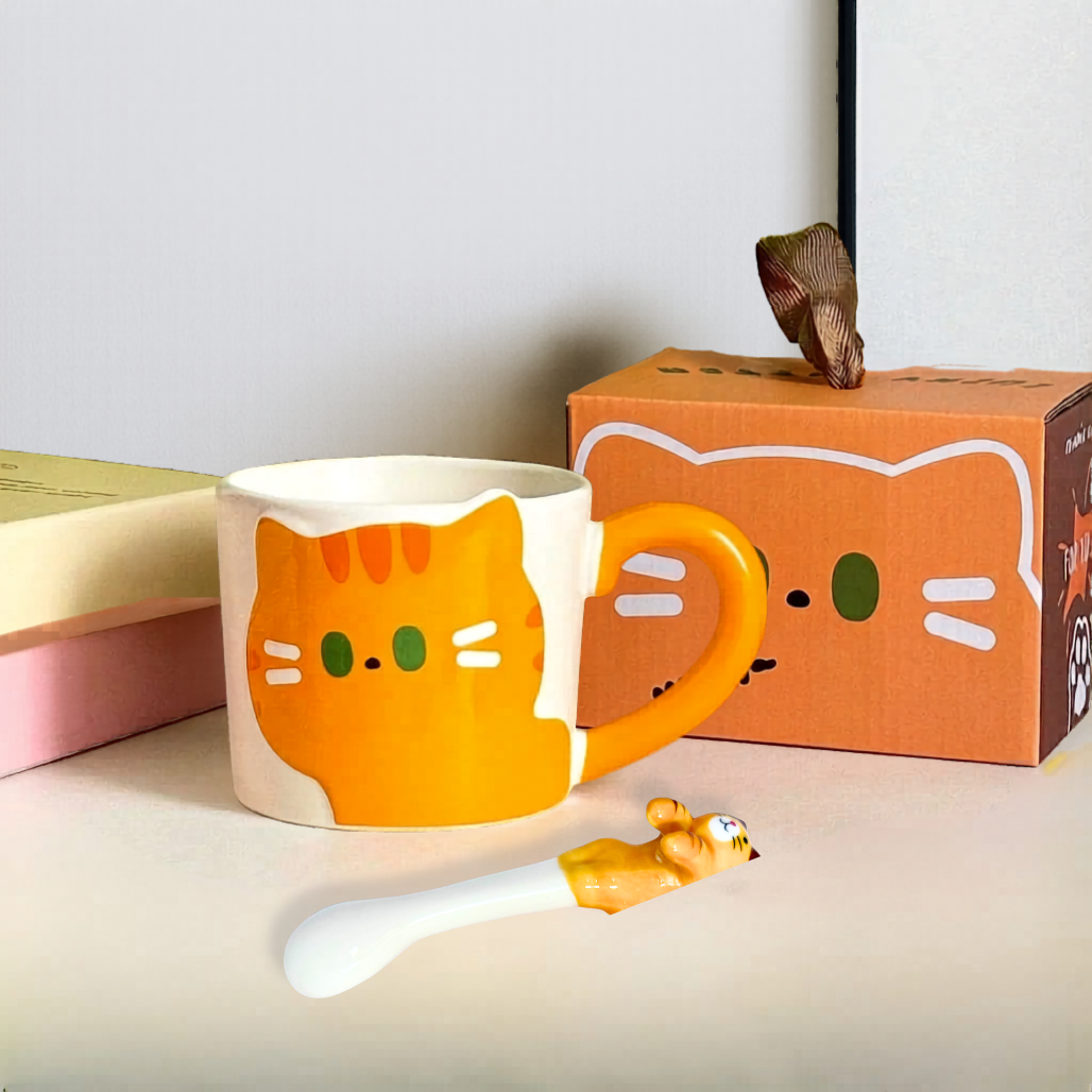 Cat-shaped mug with matching spoon and packaging on a light surface.