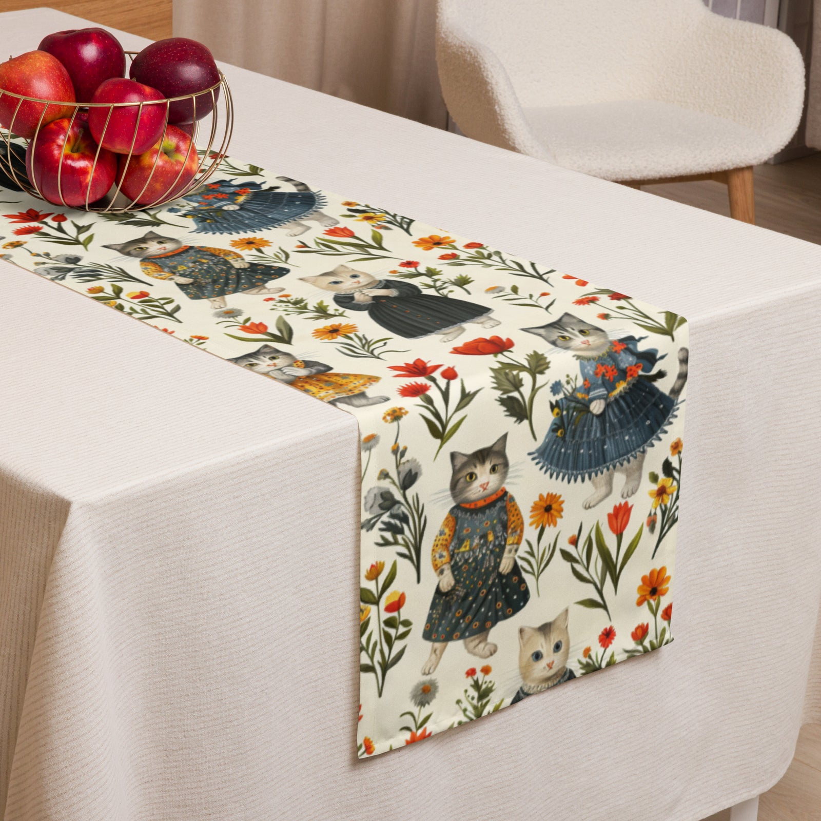 Cottage Core Cats silly pattern of cats wearing dresses in wildflowers. Table runner sits on a cream tablecloth near a basket of apples