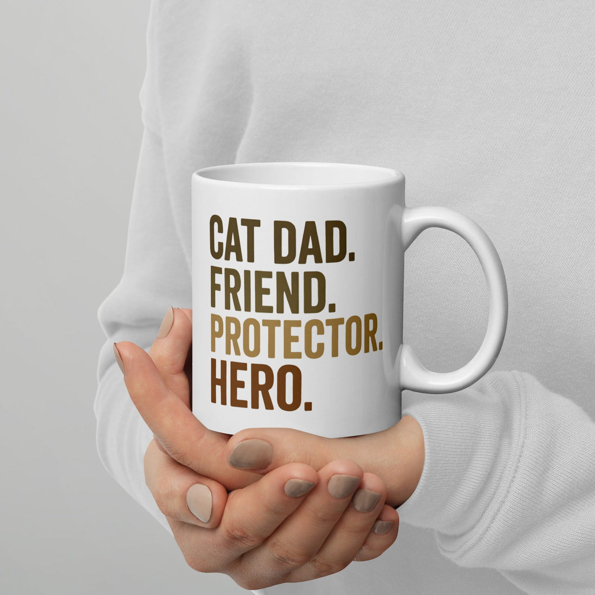 person holding white mug that says cat dad, friend, protector, hero