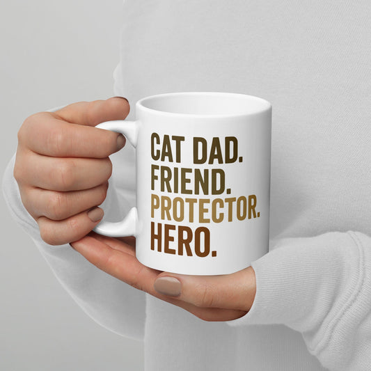 person holding white mug that says cat dad, friend, protector, hero