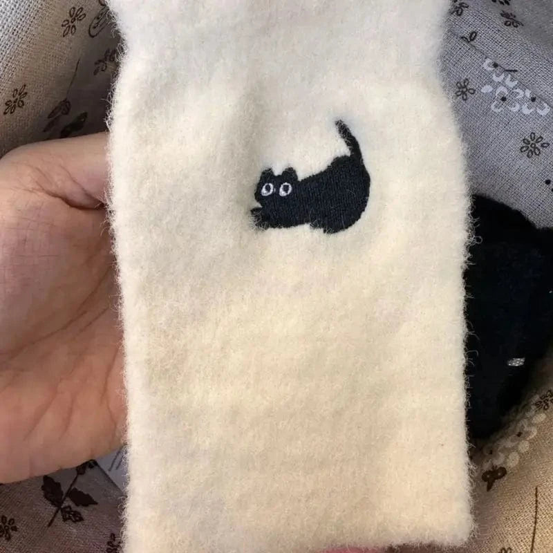 Person holding white fuzzy sock with embroidered black cat