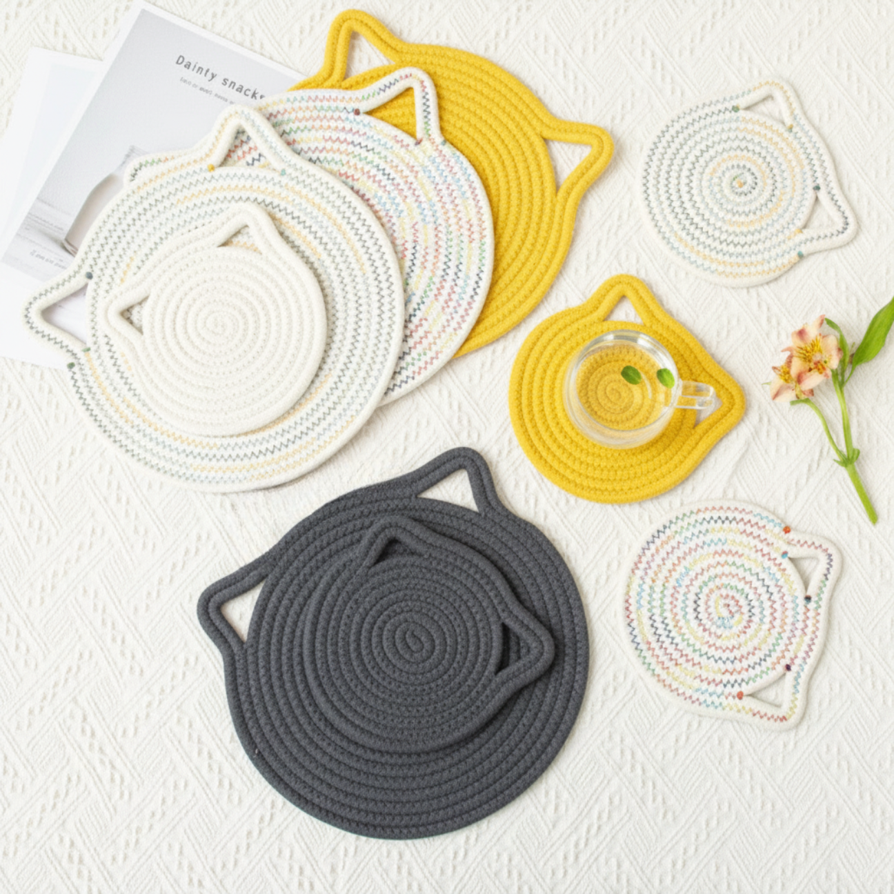 Set of cat-shaped coasters and trivets in yellow, dark gray, multi, and Rainbow multi variations on a textured surface.