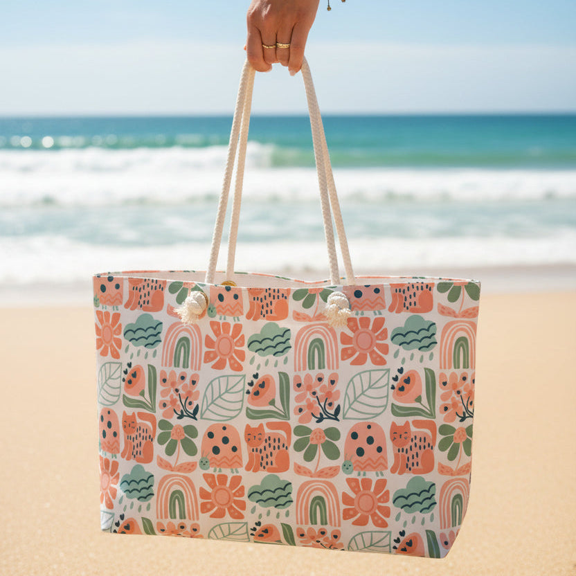 Oversized tote bag with rope handles being carried by a hand with the beach in the background.