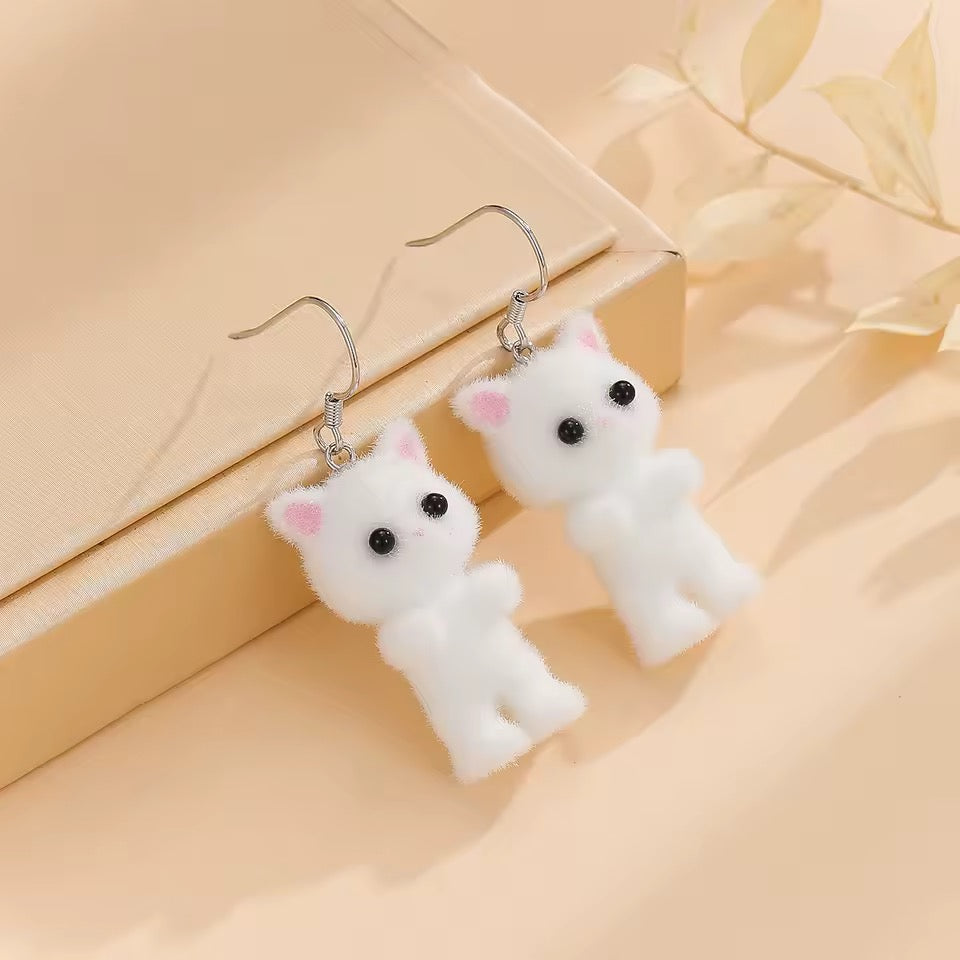White cat-shaped earrings on a beige background